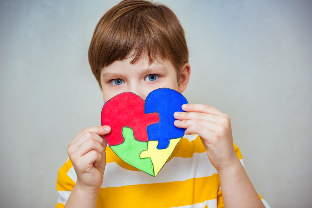 The image shows a young boy's hands tenderly holding a heart-shaped puzzle. The puzzle pieces inside the heart shape are drawn in bright, colorful marker strokes, giving the heart a handmade, expressive quality. This image symbolizes how tailored, empathetic approaches can help unlock the remarkable potential within every child, including those on the autism spectrum or with other cognitive differences.