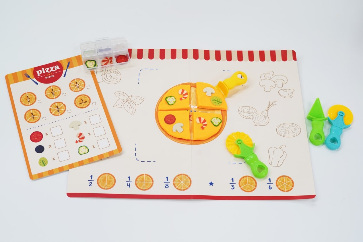 The image shows an array of colorful, educational toys and materials related to pizza and fractions from the Pizza Maths STEM box. There is a plastic pizza with removable slices, a pizza menu with various toppings and fraction markings, and drawing/coloring pages with pizza-themed illustrations. Additionally, there are child-friendly utensils like a play knife and fork.