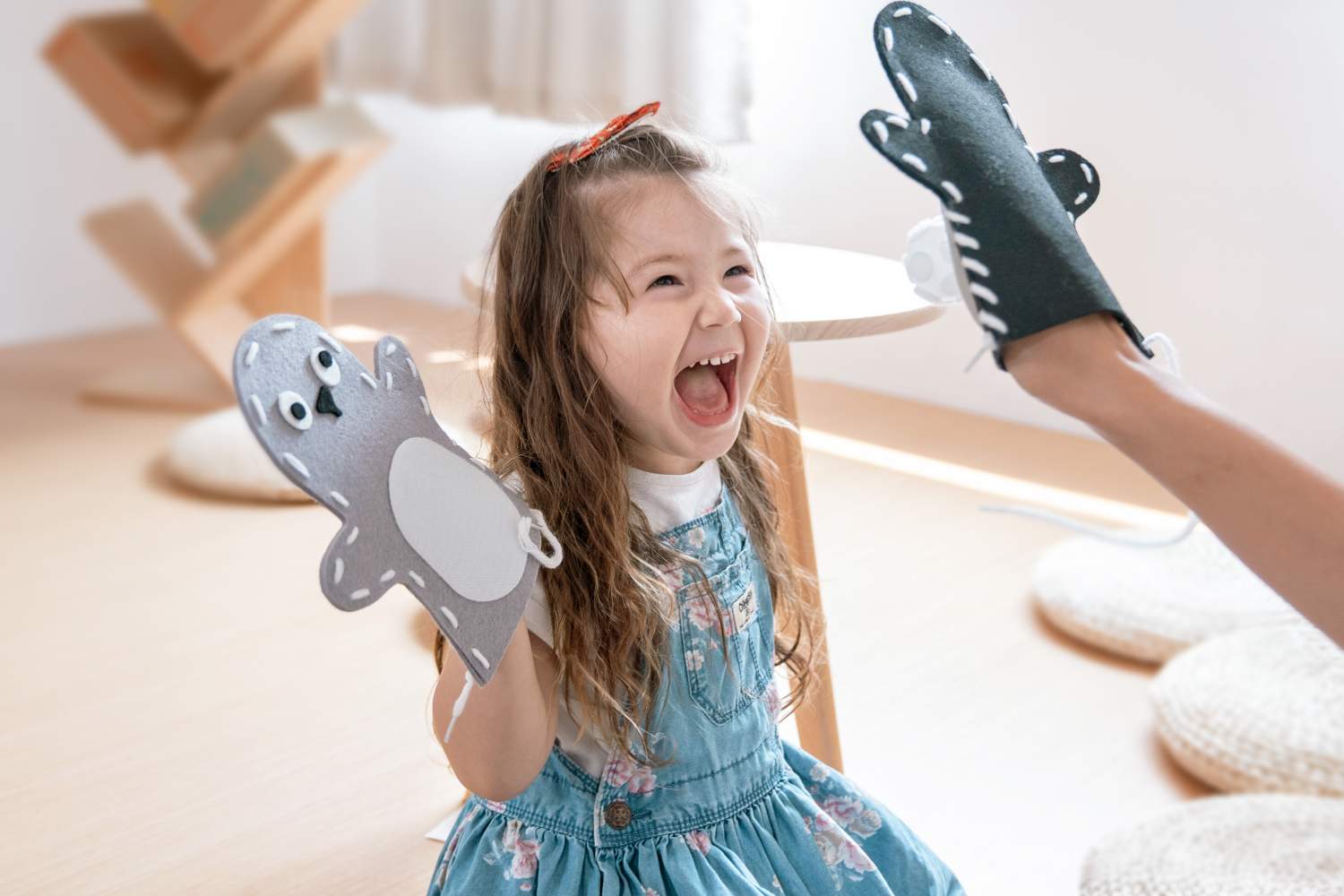 A young girl laughs happily while playing with hand puppets.