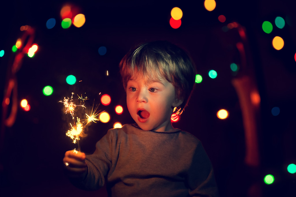 A toddler holding a sparking firework, looking at it with wonder and amazement, feeling joyful and excited