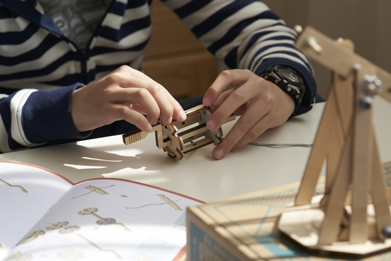 A child's hands carefully assemble a toy, their focus intense as they work on the intricate details. The scene is filled with a sense of quiet concentration and the joy of creation, suggesting the child's passion for building and learning through hands-on experience.